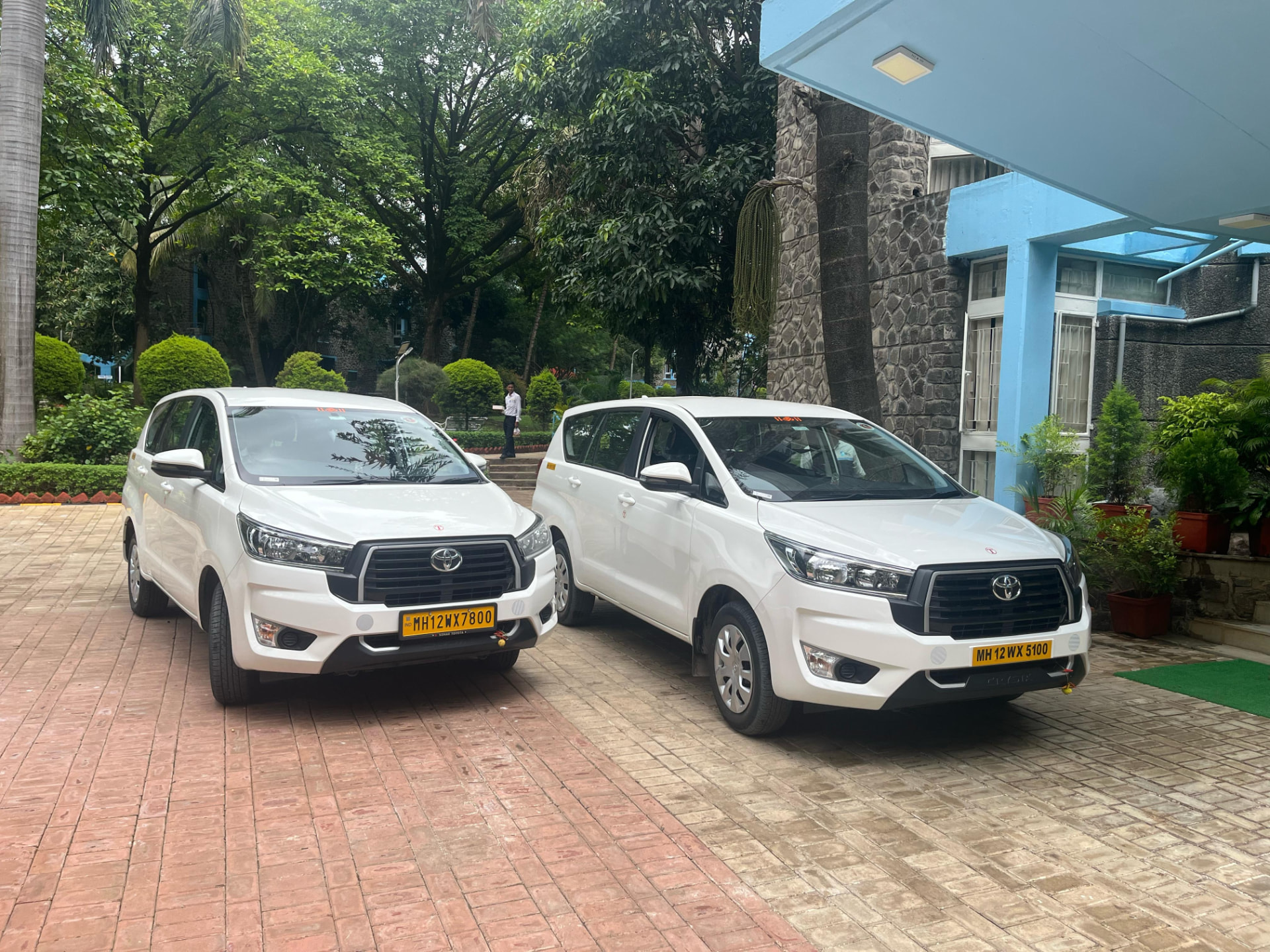 Two white Om Travels Innova Crysta cars at a corporate campus in Pune